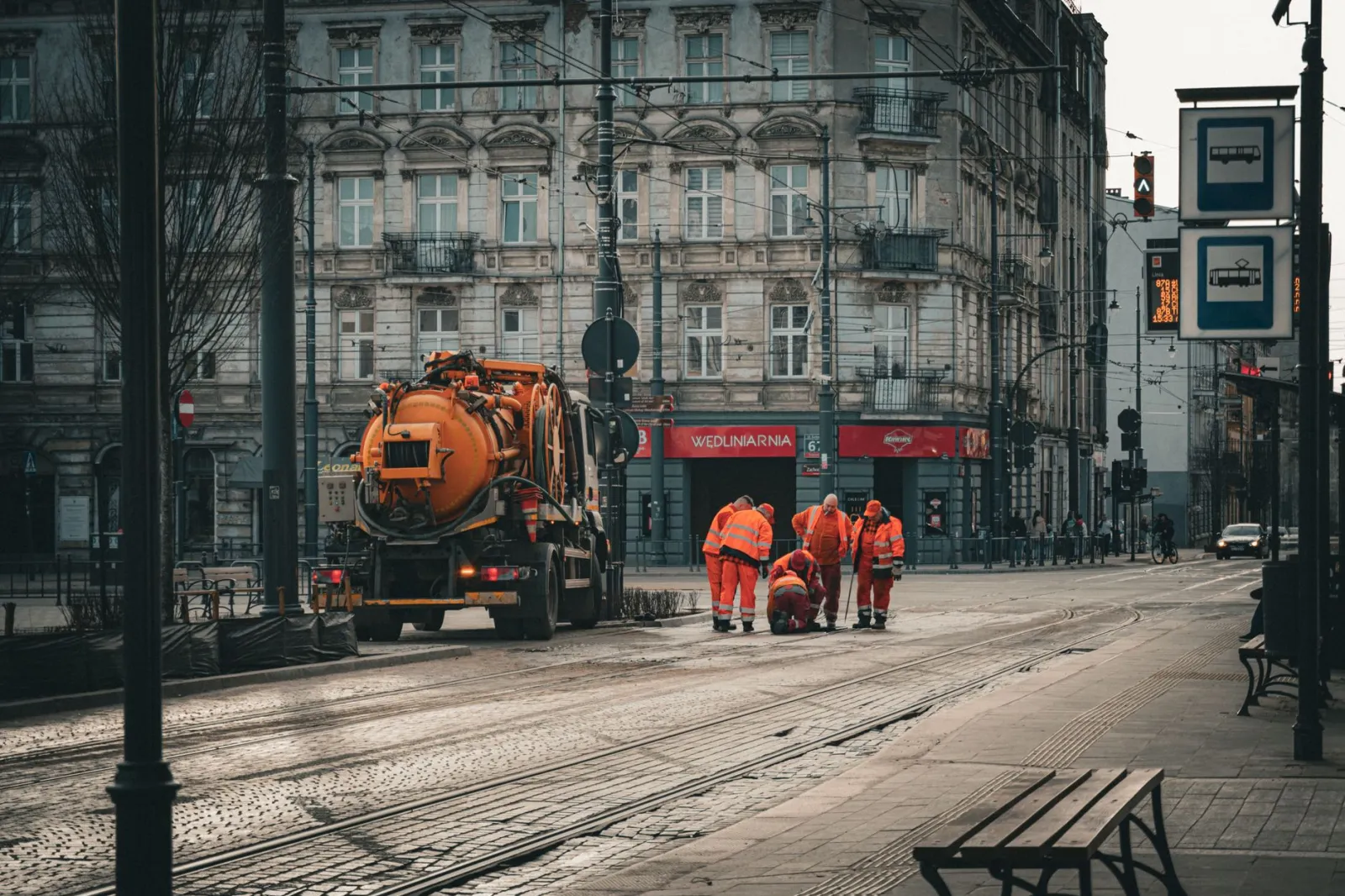 Prace przy torowisku tramwajowym z pracownikiem i tramwajem w tle