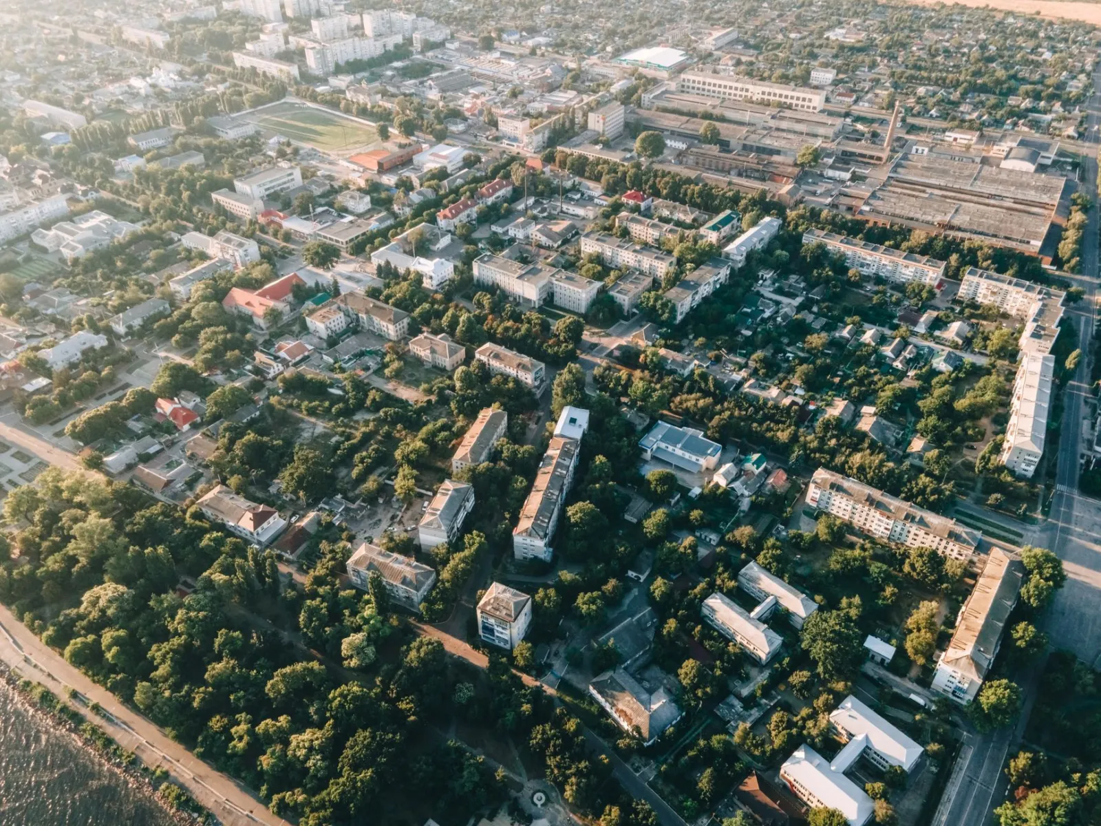 Widok z lotu ptaka na mieszany obszar miejski z blokami, niską zabudową i zielonymi skwerami.