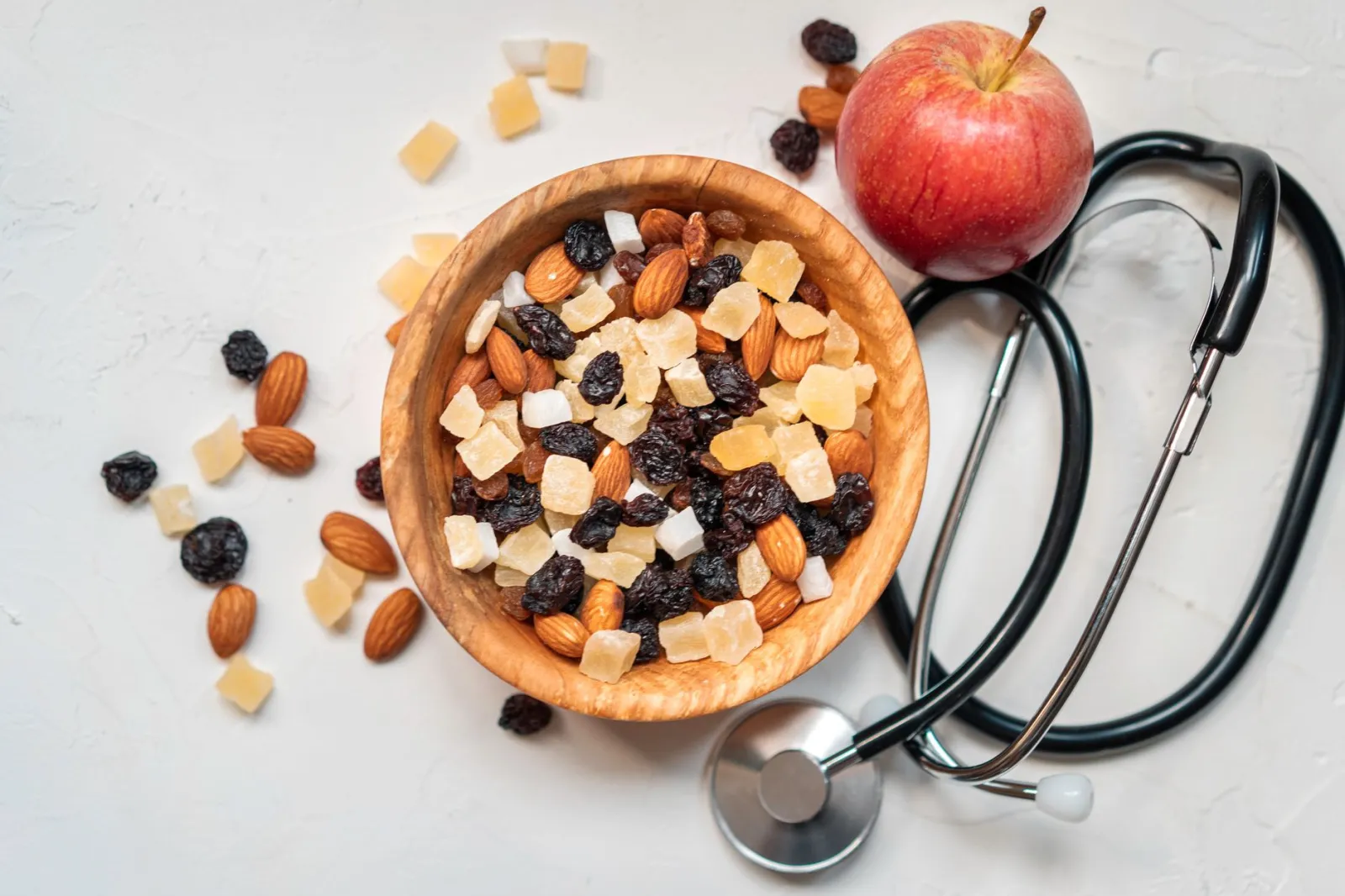 Top view of a mixed nut and dried fruit bowl with an apple and stethoscope, emphasizing healthy eating.