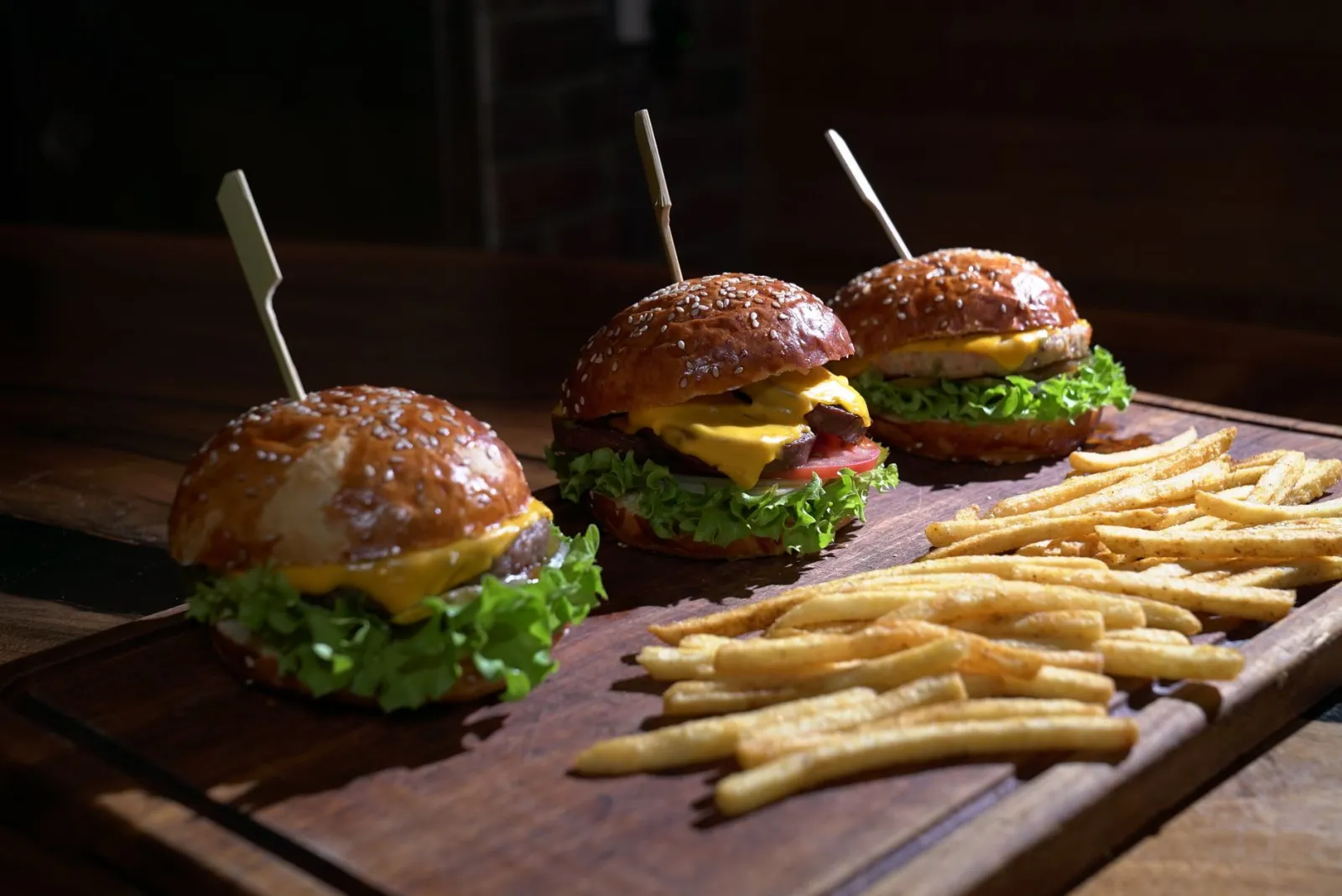 Three juicy cheeseburgers with lettuce, tomato, and fries on a wooden platter.