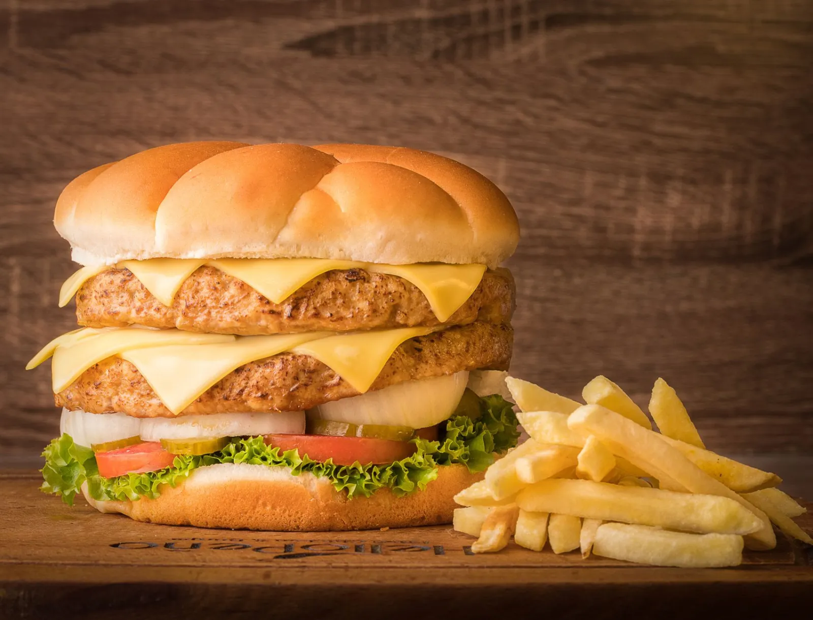 Duży burger z podwójnym kotletem i porcją frytek na stole